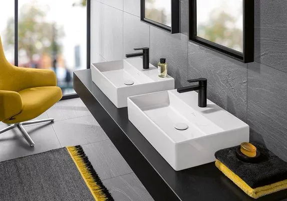 Twin basins on a long counter in a bathroom with a yellow armchair